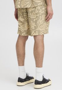 Linase segu segavad lühikesed püksid helepruunis toonis, lehvikmustriga, tasapinnaliste esitaskute ja mugava lõikega. Sobitatud mustade tossude ja valgete sokkidega.