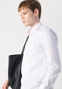 White, patterned shirt with a herringbone texture, featuring a collar and buttons, paired with a black leather tote bag.