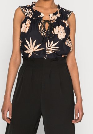 Blusa nera floreale con scollo arricciato e maniche a cappuccio. Presenta motivi di foglie arancioni e una cravatta centrale con dettagli neri testurizzati.