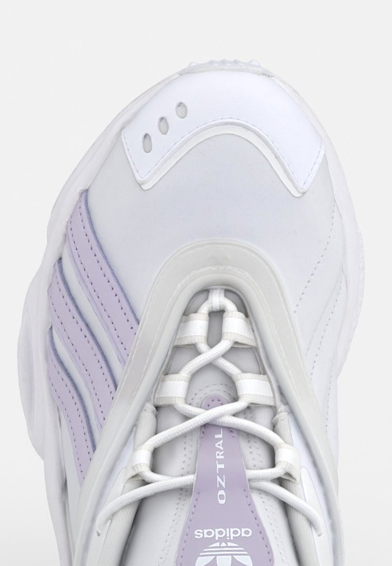 Sneaker bianco con accenti lavanda, con tomaia sintetica, lati testurizzati e un sistema di allacciatura distintivo, vista dall'alto.
