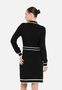 Robe noire en tissu tricoté avec de longues manches, présentant des rayures horizontales blanches aux poignets et à la taille. Design de col classique.