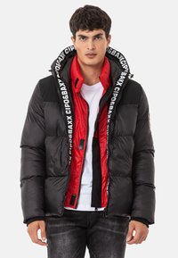 Daunenjacke mit schwarzem Außenmaterial, rotem Innenfutter und kontrastierender schwarzer Markenbeschriftung an der Kapuze. Mit Reißverschluss und seitlichen Taschen.
