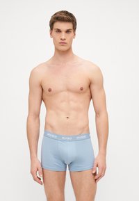 Helle blaue Boxershorts aus weichem Stoff, mit einem grauen Bund, auf dem das "HUGO"-Logo in Weiß abgebildet ist, liegen an einem model ohne Shirt.