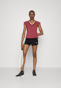 Camisa atlética color burdeos con cuello en V y mangas cortas, combinada con pantalones cortos negros. Zapatillas de tenis negras y una raqueta blanca completan el conjunto.