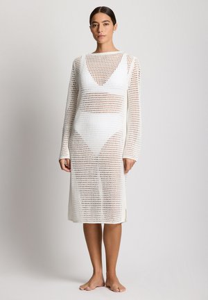Biała sukienka szydełkowa o konstrukcyjnym kroju, z długimi rękawami i długością do połowy łydki. Wzór składa się z otwartych, dzianych fragmentów.