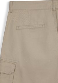 Pantaloni cargo beige con una tasca posteriore e una tasca laterale a pattina, realizzati in robusto tessuto di cotone con una texture liscia e cuciture rinforzate.