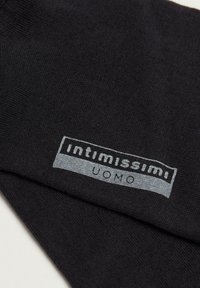 Schwarze Socken aus weichem Stoff mit einem grauen Logopatch, auf dem "intimissimi" und "UOMO" steht, platziert nahe der Oberseite.