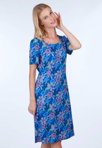 Kurzärmliges Kleid aus blauer Stoff mit floralem Muster und lila sowie grünen Akzenten, runder Ausschnitt und knieumspielende Länge.