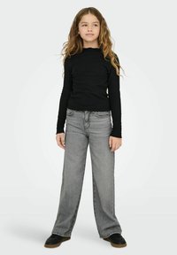 Juodas ilgas rankovėmis megztinis su banguotu iškirpimu, derinamas su laisvais pilkais džinsais. Juodi sportbačiai užbaigia aprangą.