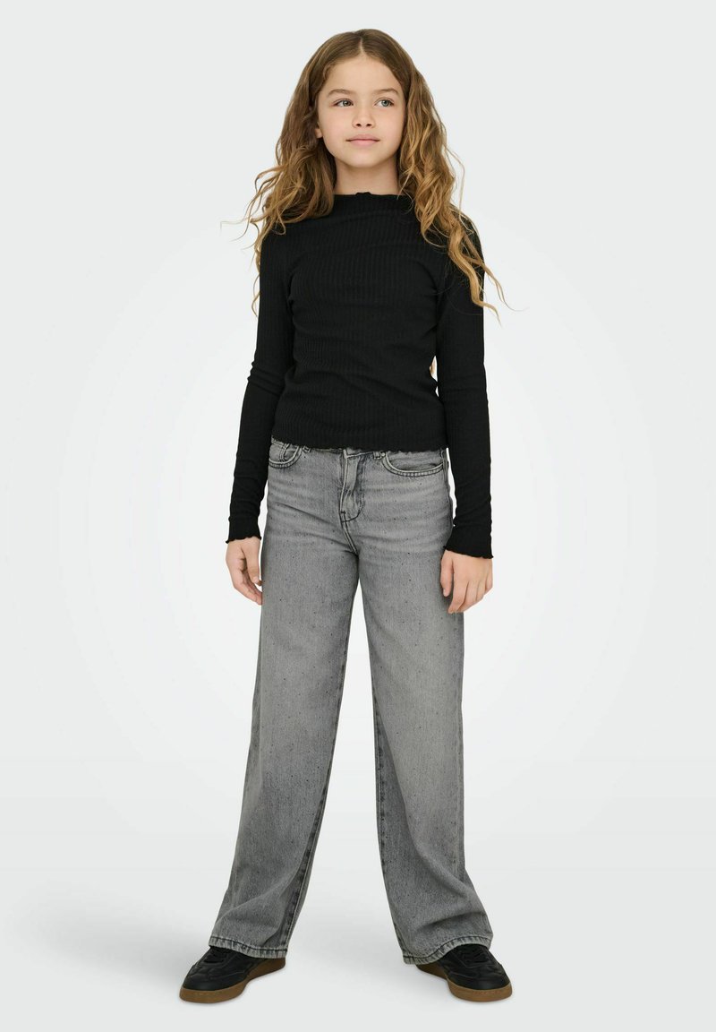 Juodas ilgas rankovėmis megztinis su banguotu iškirpimu, derinamas su laisvais pilkais džinsais. Juodi sportbačiai užbaigia aprangą.