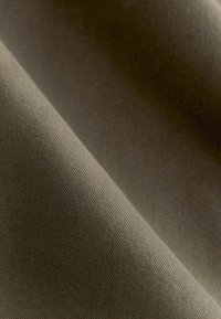 Khaki kangas sileda tekstuuriga, millel on peen kudumis muster. Materjal langeb õrnalt, omades peent sära ja sügavust.