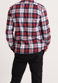 Rød, hvid og blå ternet flannel skjorte med lange ærmer, knappet krave og en buet kant, båret over sorte bukser.