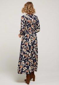 Robe longue bleu marine avec un motif abstrait beige et corail. Dotée de manches longues et d'une taille élastique, associée à des bottes à talons marron.