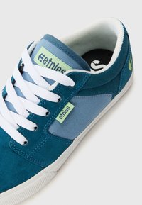 Blue and teal sneakers with white laces, featuring a mix of suede and canvas materials, and a green logo accent on the side.