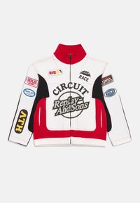 Rød, hvit og svart racingjakke med høy krage, med grafiske logoer og lapper, glidelås og kontrastsøm.