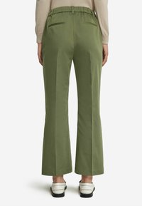 Gröna vida byxor med hög, elastisk midja och två bakfickor; slät textur och skräddarsydd design. Bärs med vita skor.