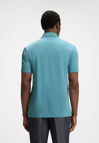 Turkusowa koszulka polo z krótkim rękawem, płaskim kołnierzykiem i bocznymi rozcięciami. Gładki materiał bawełniany, jednolity wzór i luźny krój.