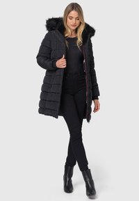Black puffer jacket with a fur-trimmed hood, quilted design, zippered front, and side pockets. Worn with black skinny jeans and ankle boots.
