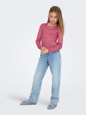 Różowy, dopasowany top z długim rękawem; jasnoniebieskie, wysokie dżinsy; miękkie niebieskie baleriny z kokardką. Prosty, casualowy strój na jasnym tle.