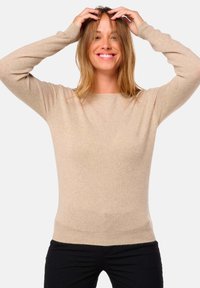 Pull en laine beige avec un col rond et des manches longues. Texture douce, design ajusté et ourlet côtelé, porté avec un pantalon noir.