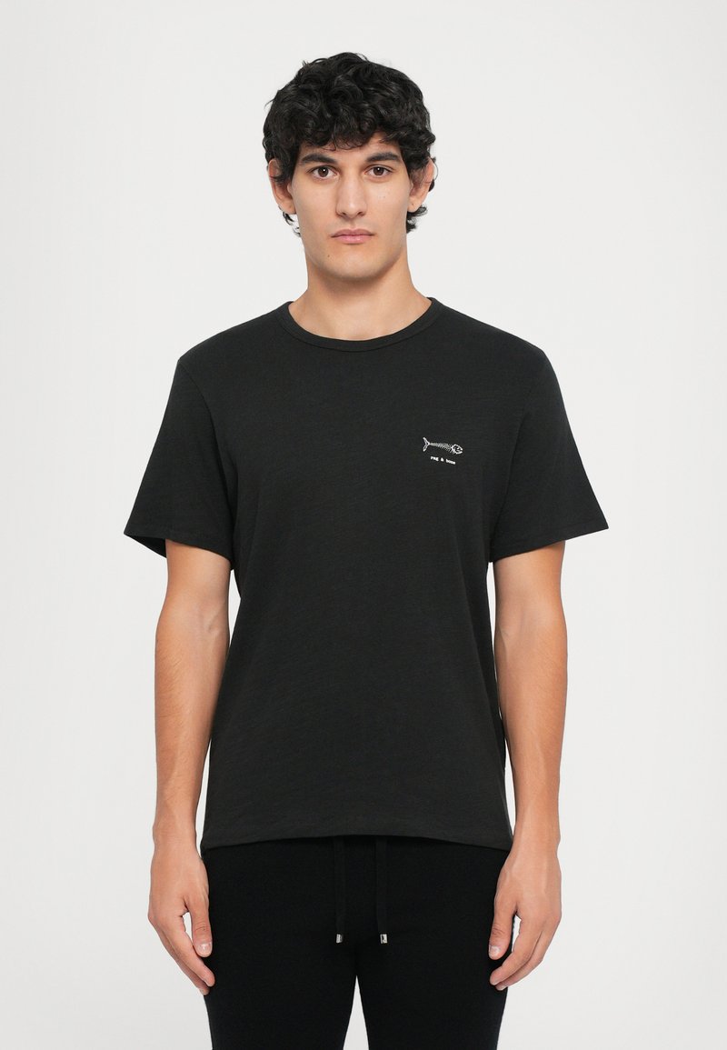 Camiseta negra en corte relajado, hecha de algodón suave. Presenta un gráfico de espina de pescado en el lado izquierdo del pecho y un escote redondo clásico.
