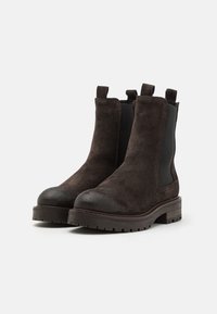 Bottines en suède marron avec des panneaux élastiques noirs sur les côtés, bout arrondi, semelle en caoutchouc texturée et languettes à l'arrière pour un enfilage facile.
