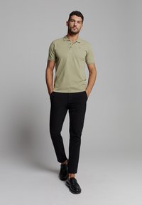 Lichtgroene polo met een kraag en drie knopen, gecombineerd met zwarte slim-fit broek en zwarte instappers.