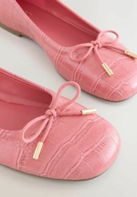 Roosad baleriinasussid tekstuurse võltskrokodillinaha mustriga, ümarate ninaosade, lipsudega ja kuldse tooniga dekoratsioonidega.