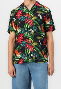 Chemise à manches courtes avec boutons, présentant un fond noir orné de motifs floraux tropicaux vibrants en rouge, vert, blanc et jaune.