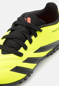Botín de fútbol amarillo brillante con cordones negros, parte superior sintética texturizada y acentos negros. Presenta tacos de goma para tracción.