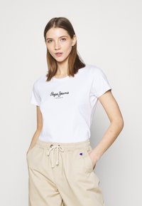 T-shirt en coton blanc à manches courtes avec un logo noir "Pepe Jeans London" centré sur la poitrine, assorti à un pantalon beige à taille élastique.