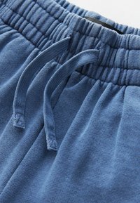 Blaue Pants mit elastischem Bund und Kordelzug, die eine weiche Textur und eine lockere Passform aufweisen. Der Stoff wirkt glatt und flexibel.