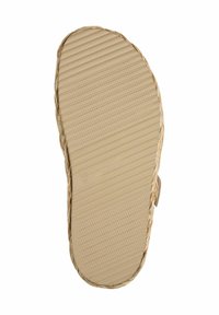 Beige sandal sole with a textured surface featuring horizontal grooves and a woven edge, emphasizing grip and flexibility.