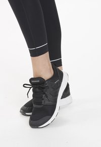 Svarta träningsskor med nät- och syntetöverdrag, rund tå och vit gummisula. Har svarta snören och "ENDURANCE"-logotyp.