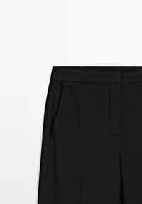 Black tailored pants with a smooth texture, featuring a flat waistband, side pockets, and minimalist design elements.