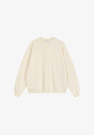 Grietos spalvos džemperis su apvaliu iškirpimu, ilgomis rankovėmis ir giliu apykaklės kraštu. Priekyje turi įspaustą tekstą "LYDANT SAULĘ".