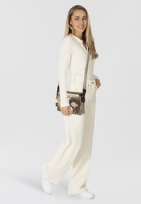 Borsa a tracolla in tessuto strutturato, con design a cartone animato, colori beige e nero, e dettagli in metallo argentato.