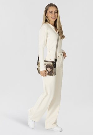 Umhängetasche aus strukturiertem Stoff mit einem Cartoon-Design in Beige und Schwarz sowie silberfarbenen Metallakzenten.