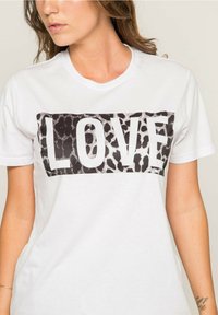 T-shirt en coton blanc avec un graphique rectangulaire imprimé léopard noir et blanc comportant le mot "LOVE" en lettres blanches en gras.