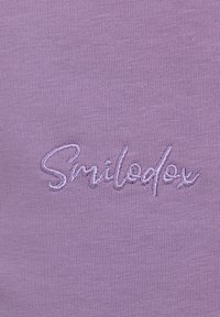 Tessuto di cotone viola con texture a righe, caratterizzato da un logo ricamato "Smiledex" in una tonalità più chiara di viola per creare contrasto.