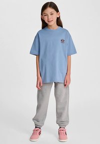 Jasnoniebieski bawełniany t-shirt z krótkimi rękawami i małym logo na piersi, zestawiony z szarymi spodniami dresowymi i różowymi trampkami.