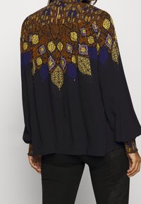 Camicia nera con yoke a fantasia colorata nei toni del blu, giallo e arancione. Presenta maniche lunghe e una vestibilità morbida. Tessuto testurizzato.