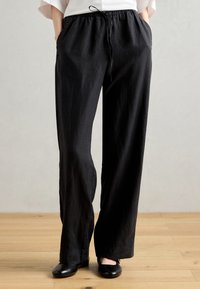 Zwarte, wijde broek gemaakt van lichtgewicht stof met een gestructureerde afwerking. Heeft een elastische tailleband en zijzakken.