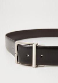 Black leather belt featuring a silver rectangular buckle and adjustable holes. The brand name is subtly embossed near the buckle.