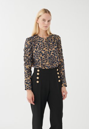 Blusa a fiori beige e blu navy, con maniche a sbuffo e scollatura rotonda. Pantaloni neri con bottoni dorati lungo la vita.