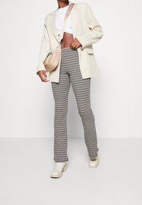 Beżowa marynarka, biała krótka bluzka, prążkowane spodnie w czarno-kremowe paski oraz beżowe botki na obcasie. Torba w dopasowanym jasnym beżowym materiale.