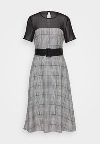 Robe à carreaux noir et blanc avec un corsage ajusté, de courtes manches transparentes, un col rond et une taille ceinturée noire.