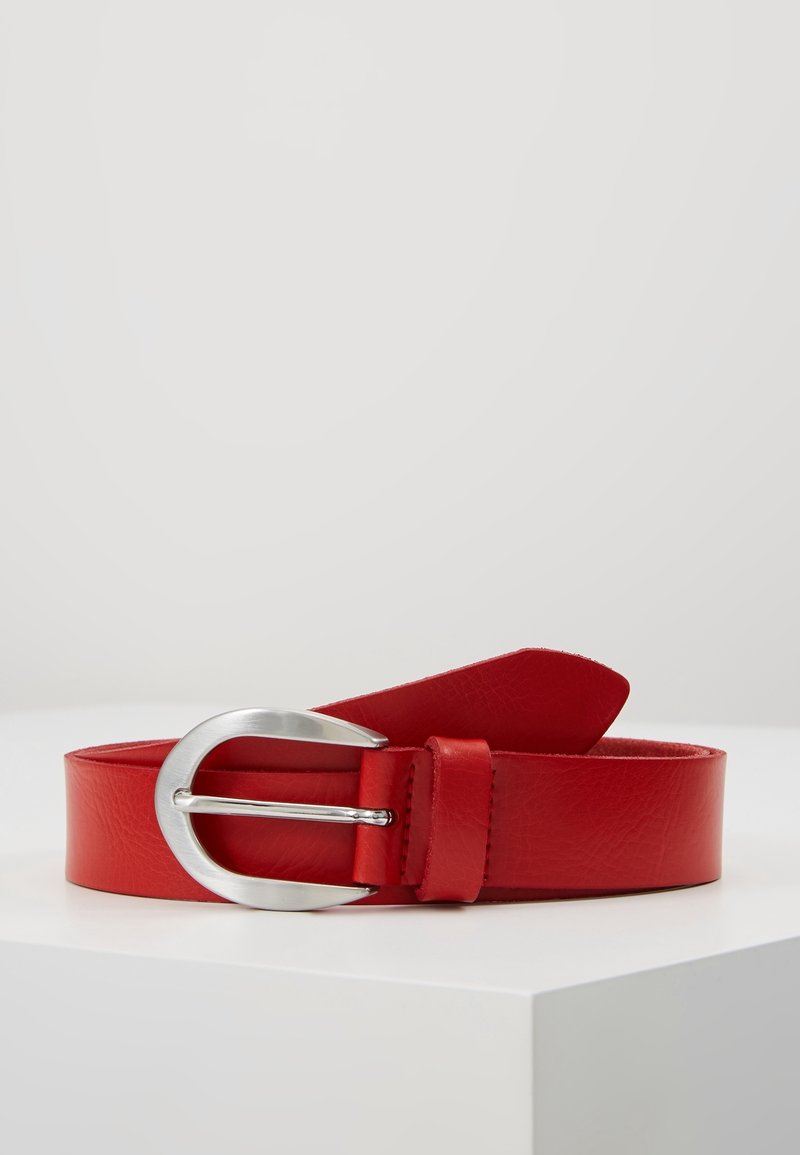 Ceinture en cuir rouge avec une boucle métallique argentée arrondie exposée sur une surface blanche sur un fond uni.