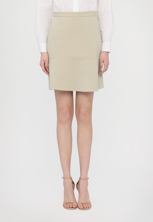 Hame panjang berwarna beige dengan bentuk terstruktur, tekstur kain yang halus, dan sabuk pinggang. Dipadukan dengan sandal hak tinggi berwarna beige dengan tali.