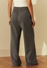 Pantaloni a gamba larga grigi realizzati in un tessuto morbido e testurizzato. Presentano una vita elasticizzata e una sola tasca posteriore. Design lungo fino al pavimento.